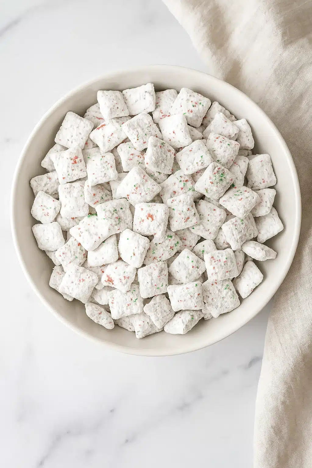 Bowl of Holiday Puppy Chow with red and green sprinkles on a white-gray table