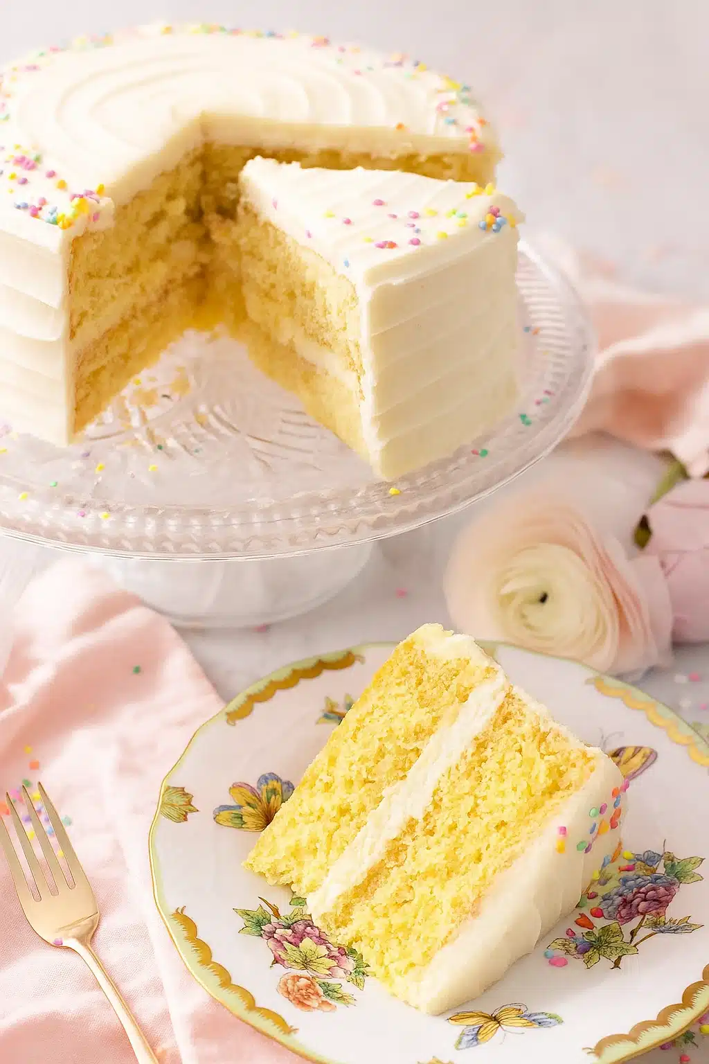 Vanilla cake recipe with buttercream frosting and colorful sprinkles on a glass stand
