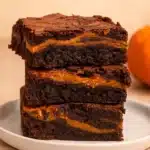 Stack of fudgy pumpkin brownies with chocolate and pumpkin swirl on white plate