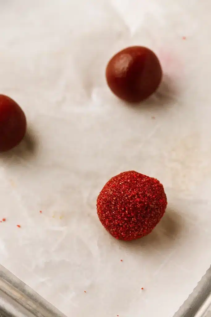 Red Velvet Blossoms Cookies – Easy, Festive & Delicious 16 Red Velvet Blossoms Cookies dough balls coated in red sugar on parchment paper