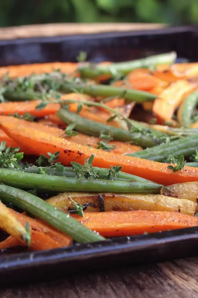 Roasted carrots and green beans on a baking sheet with herbs
