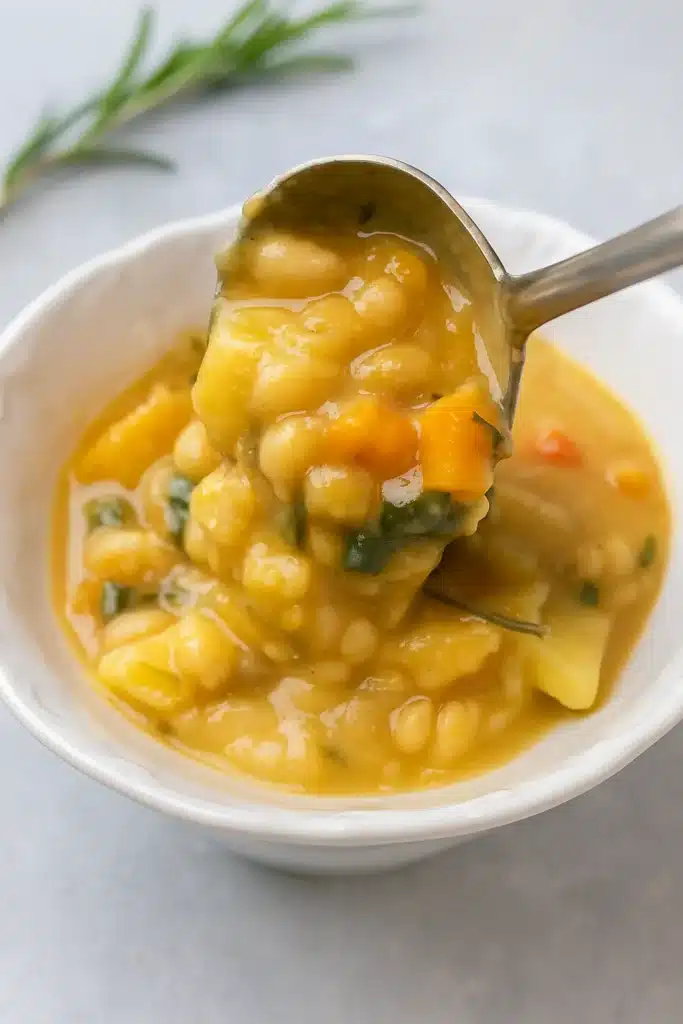 The Best White Bean Soup being served from a ladle into a bowl on a white-gray table