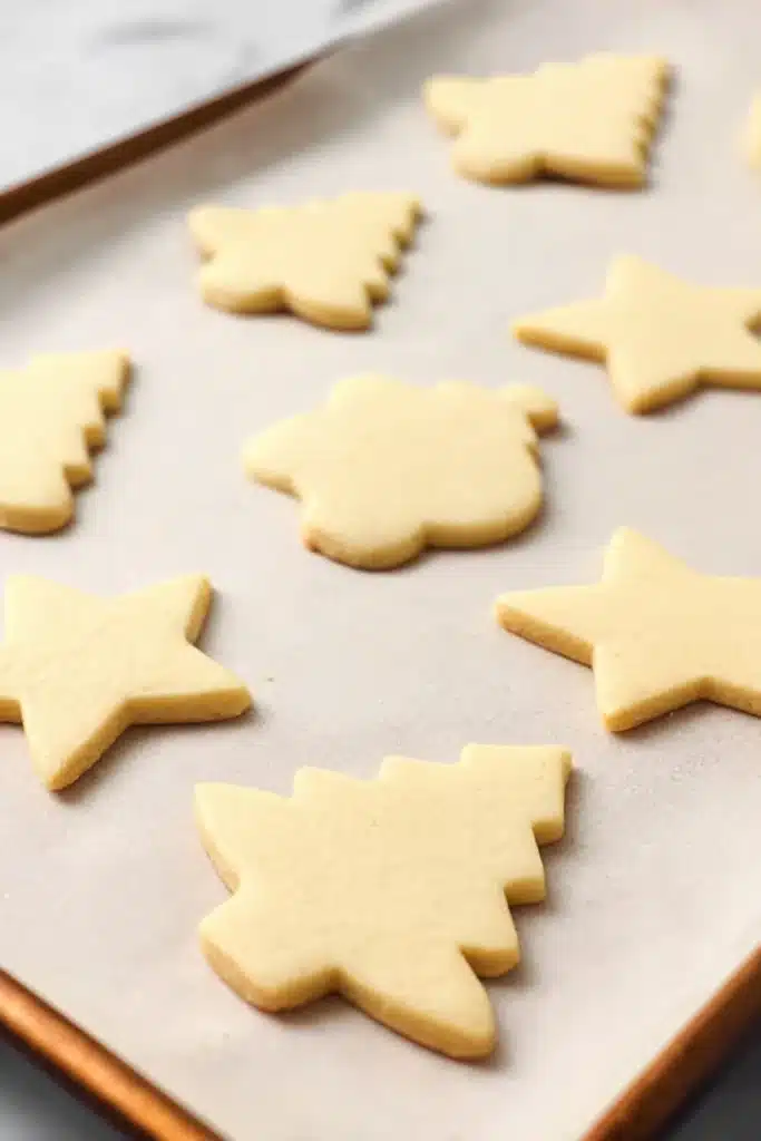 Baked vegan sugar cookies on a parchment-lined tray in star and tree shapes.