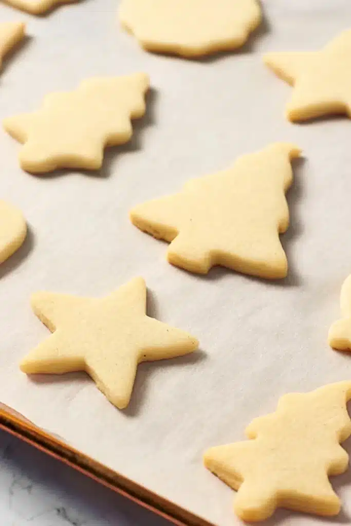 Baked vegan sugar cookies on a parchment-lined tray in star and tree shapes.