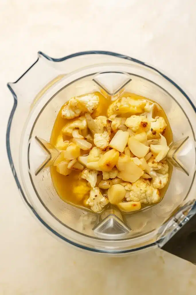 Blender filled with roasted cauliflower and garlic for cheddar cauliflower soup