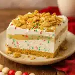 Festive lasagna dessert bar with whipped cream, sprinkles, and cookie crumble on a white plate
