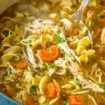 Homemade chicken noodle soup with carrots, egg noodles, and herbs in a blue pot
