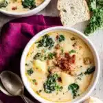 Creamy Zuppa Toscana soup with sausage, potatoes, and kale in bowls beside crusty bread