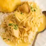 Creamy crock pot chicken and gravy over rice with biscuit on white plate