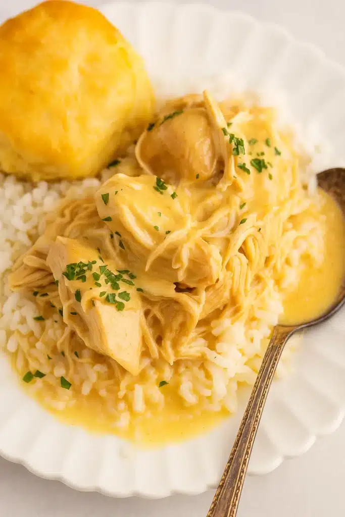 Creamy crock pot chicken and gravy over rice with biscuit on white plate