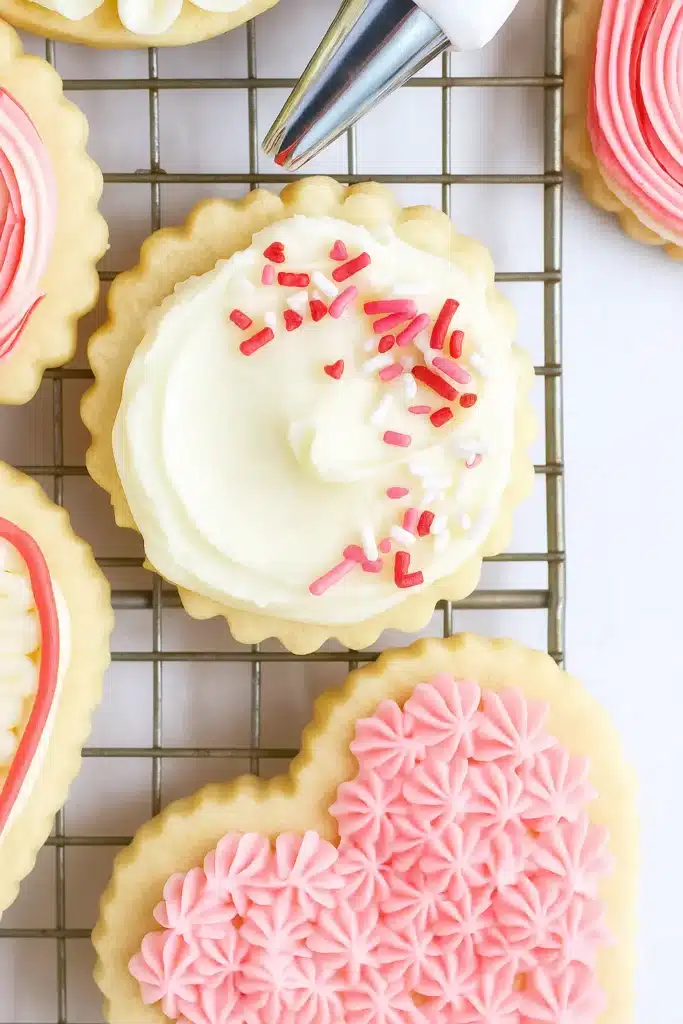 Decorating buttercream sugar cookies with white frosting and pink sprinkles