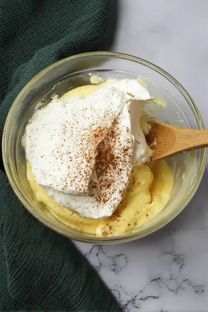 Eggnog Pie Recipe | Creamy, Easy & Irresistible Christmas Dessert 18 Folding whipped topping into eggnog pudding with a wooden spoon