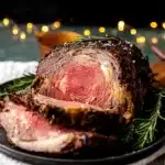 Garlic herb prime rib roast sliced on a plate with rosemary and crispy crust