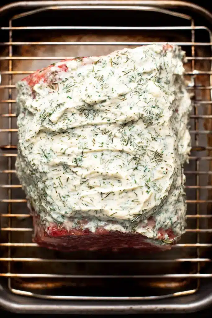 Prime rib coated with garlic herb butter on roasting rack