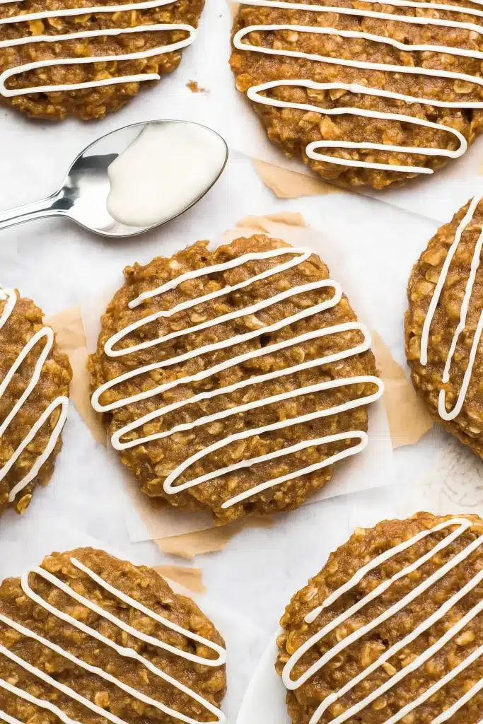 Gingerbread Oatmeal Cookies: Amazing Soft Holiday Treats 10 Gingerbread oatmeal cookies with white icing drizzles on parchment paper