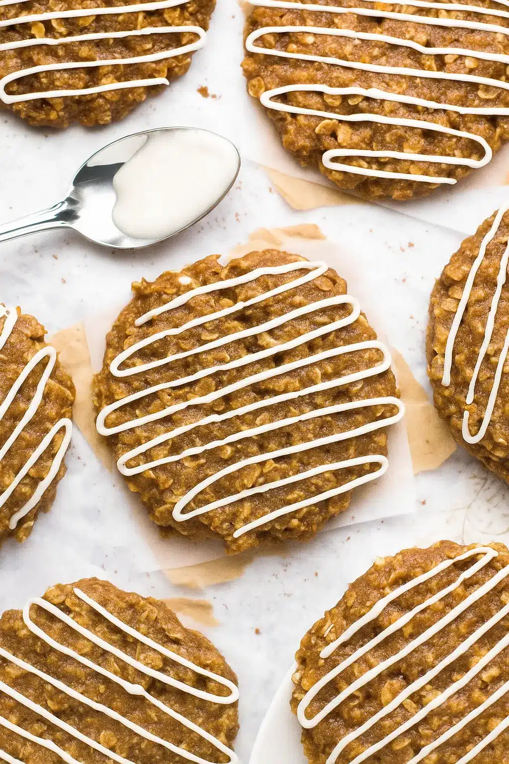 Gingerbread oatmeal cookies with white icing drizzles on parchment paper