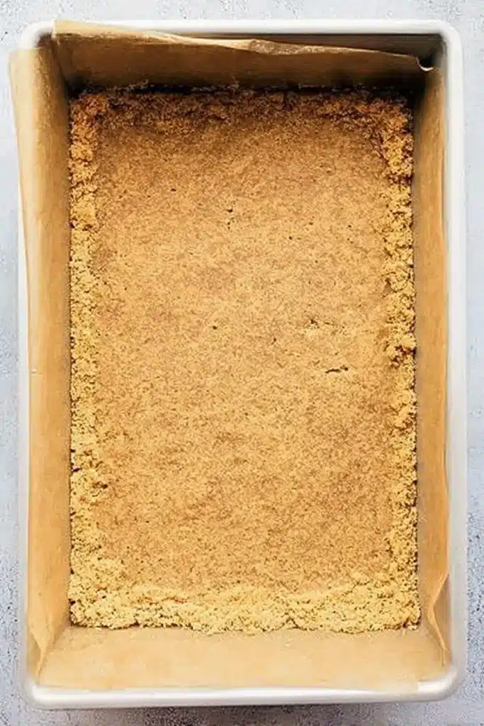 Pumpkin Cheesecake Bars | Amazing Creamy Fall Treat 17 Pressed graham cracker crust in a parchment-lined baking pan