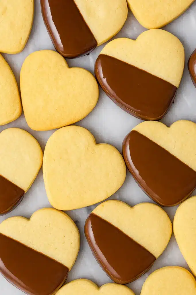 Heart-shaped shortbread cookies dipped in dark chocolate on marble surface