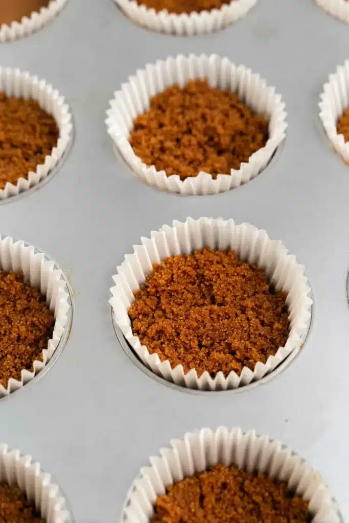 Biscoff cookie crust in muffin pan for mini gingerbread cheesecakes
