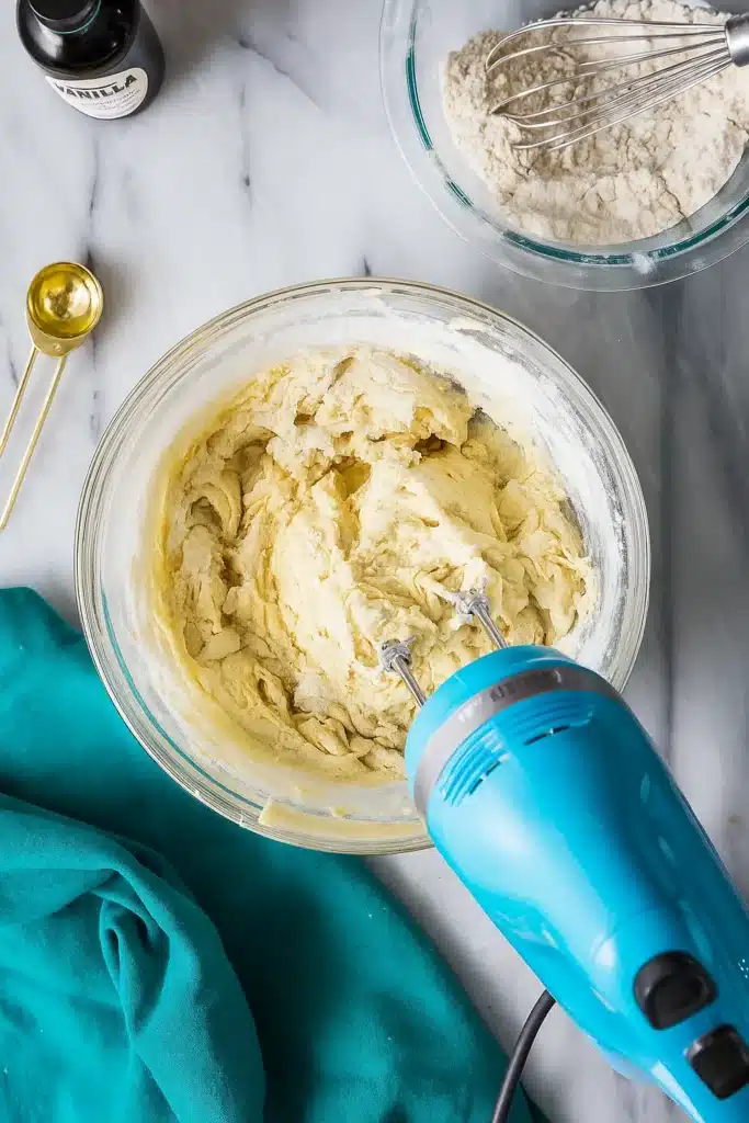 Mixing Italian cookie dough with a blue hand mixer in a glass bowl