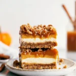 Stacked pumpkin cheesecake bars with streusel topping and caramel drizzle on a white plate