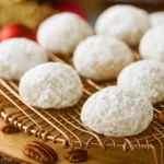 Snowball cookies coated in powdered sugar on a golden cooling rack
