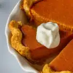 Sweet potato pie slice with whipped cream in white pie dish