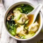 Warm bowl of wonton soup with bok choy, mushrooms, and scallions in golden broth