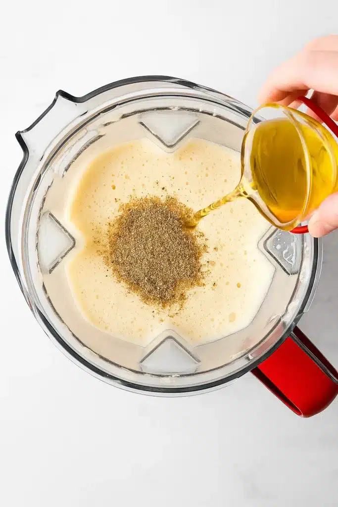 Pouring brandy into blender with homemade eggnog and nutmeg on white marble