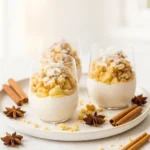 Layered baked apple crumble on cinnamon cream in glass dessert cups