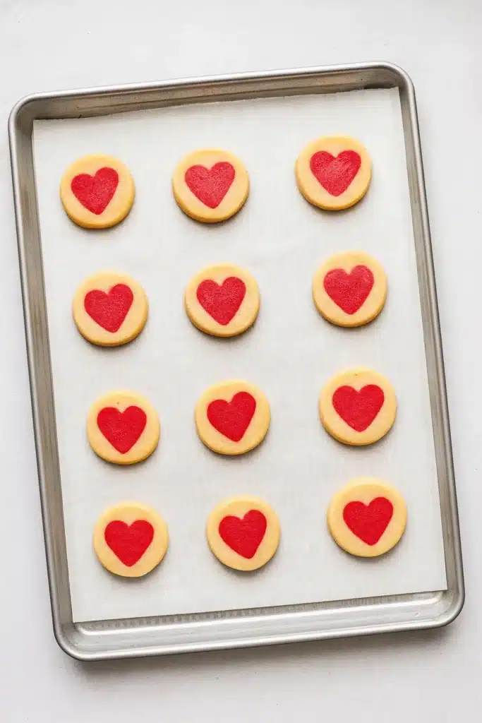 Slice and Bake Heart Cookies | Easy Valentine’s Recipe 13 Unbaked slice and bake heart cookies arranged on parchment-lined baking tray on white-gray surface