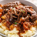 Beef bourguignon served over creamy mashed potatoes with carrots and herbs