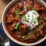 Best Award Winning Texas Chili in a white bowl with sour cream and cilantro on a dark blue napkin