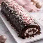 Best Christmas Peppermint Roll Cake topped with crushed peppermint on white plate