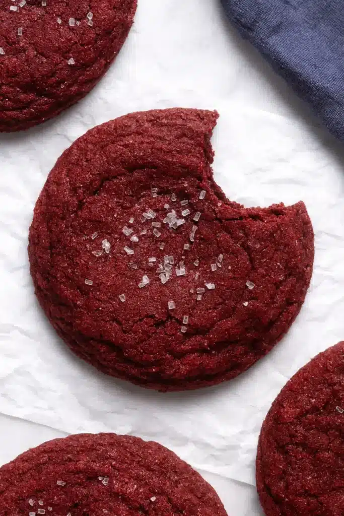 Red Velvet Cookies Recipe | Soft, Chewy & Amazing Treat 13 Bitten red velvet cookie showing soft chewy texture on parchment paper