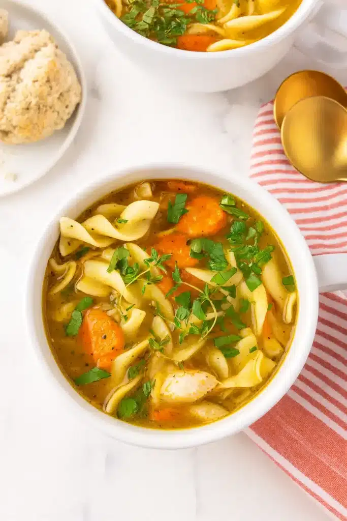 Two bowls of chicken noodle soup with egg noodles and red napkin