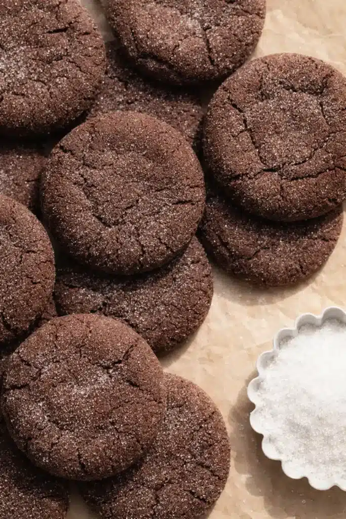 Chocolate sugar cookies on parchment with sugar bowl beside them