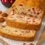 Freshly baked cranberry nut bread loaf with sliced pieces on wooden board