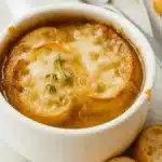 Golden French onion soup with melted Gruyere and toasted bread in a white bowl