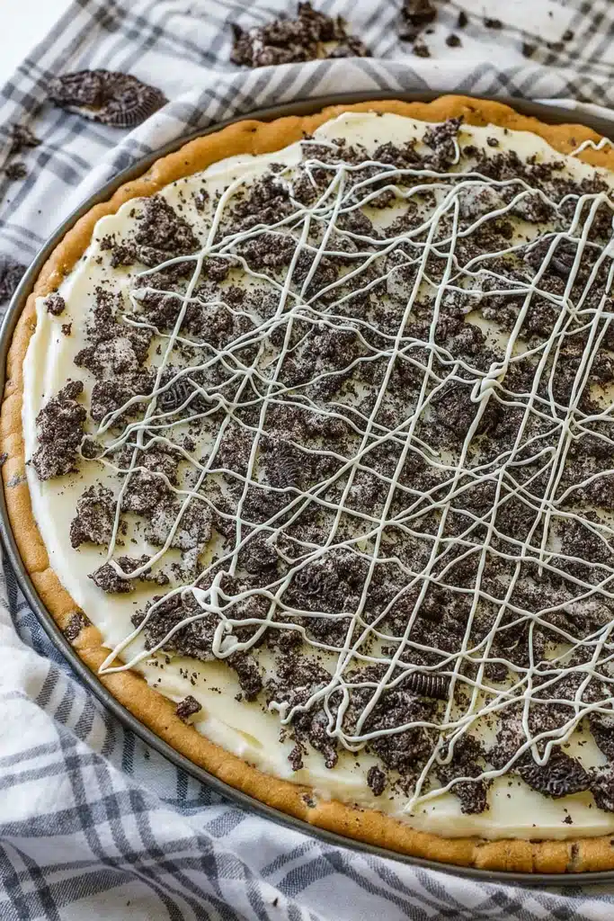 cookies and cream dessert pizza topped with Oreos and white chocolate drizzle