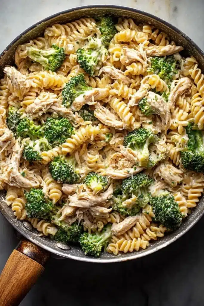 Creamy rotisserie chicken broccoli pasta in skillet with sauce and broccoli