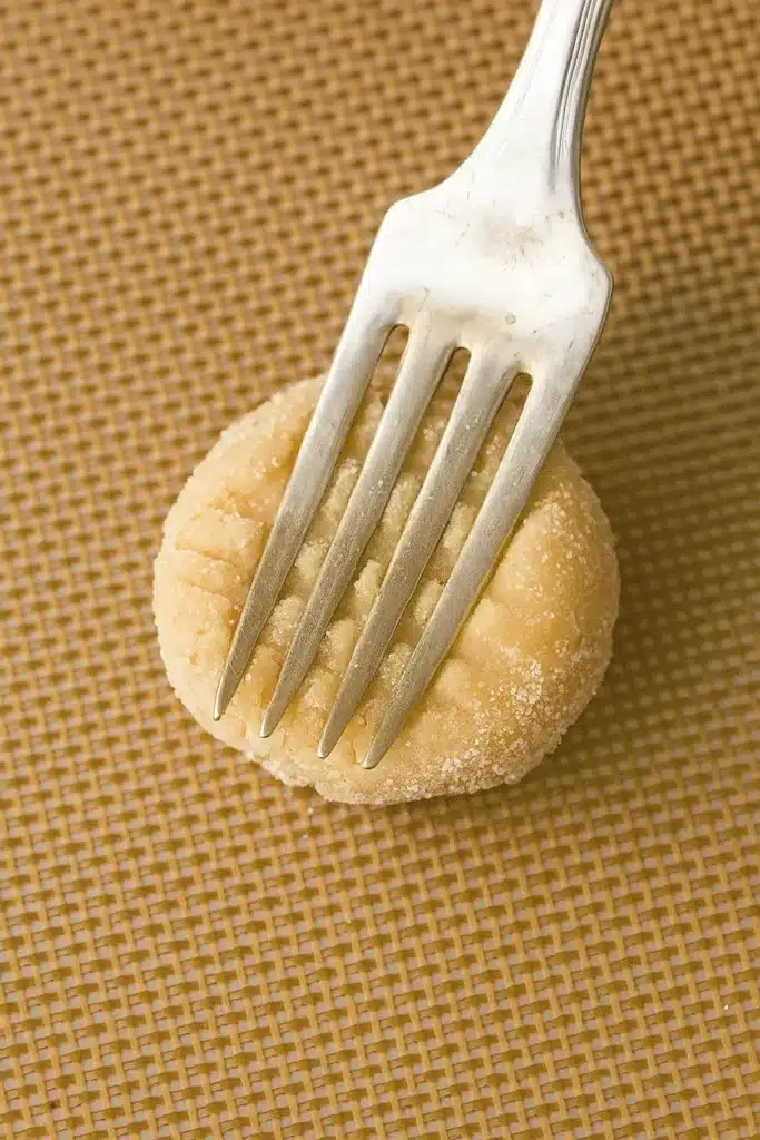 Pressing peanut butter cookie dough with a fork before baking