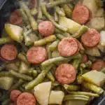 Crockpot kielbasa and green beans with potatoes steaming in black slow cooker