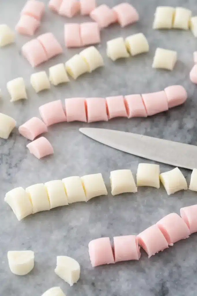 Pastel pink and white butter mints being cut on marble with kitchen knife