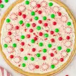 Christmas cookie pizza topped with frosting, candies, and peppermint on marble surface