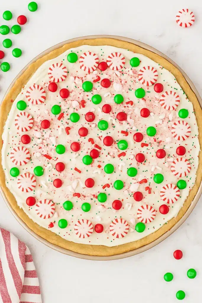 Christmas cookie pizza topped with frosting, candies, and peppermint on marble surface
