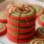 Stack of red and green Christmas pinwheel cookies tied with gold twine on a plate