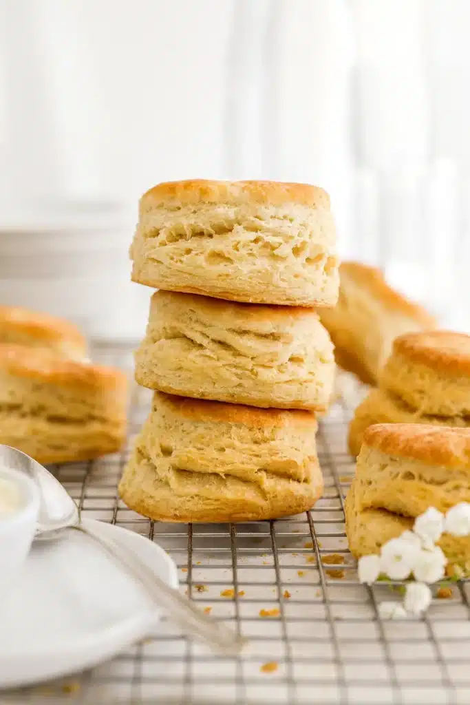 Flaky sourdough biscuits stacked on cooling rack in sunlight
