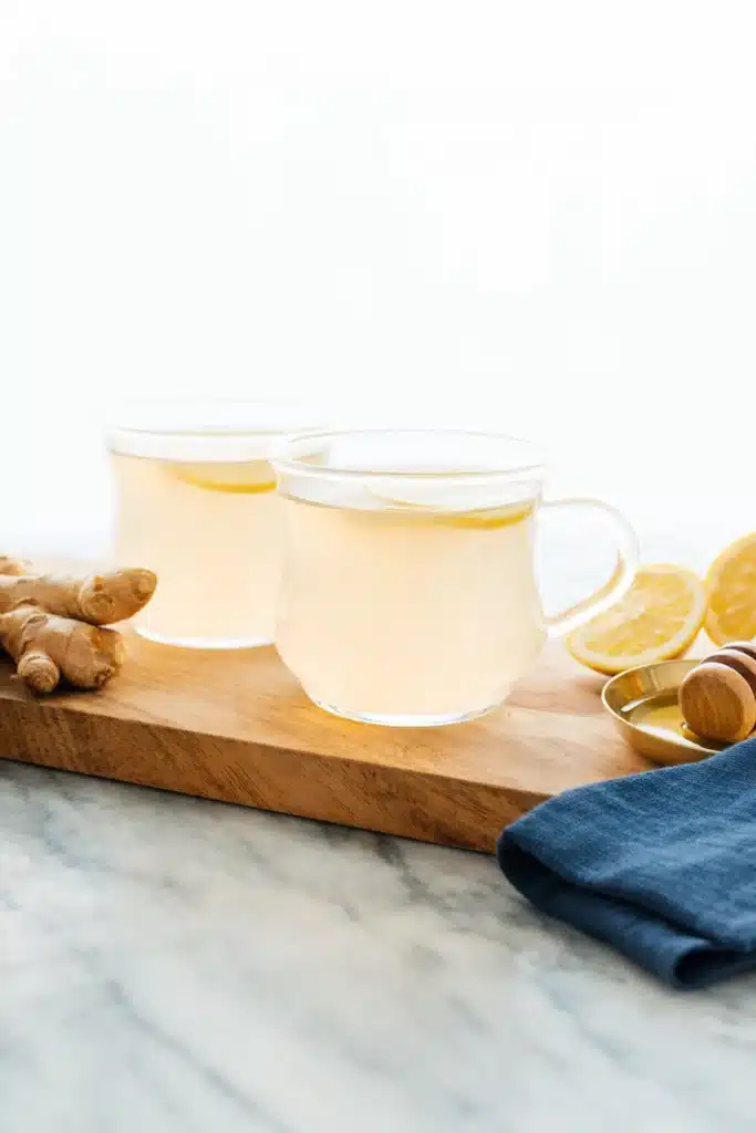 Two glass mugs of ginger lemon tea with fresh ginger and honey on marble table