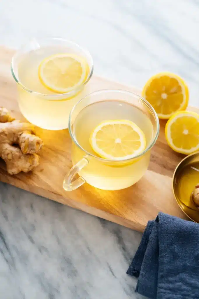 Two glass cups of ginger lemon tea with fresh ginger and lemon on a marble table